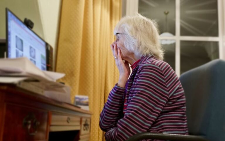 Zdjęcie przedstawia zmartwioną seniorkę patrzącą na monitor